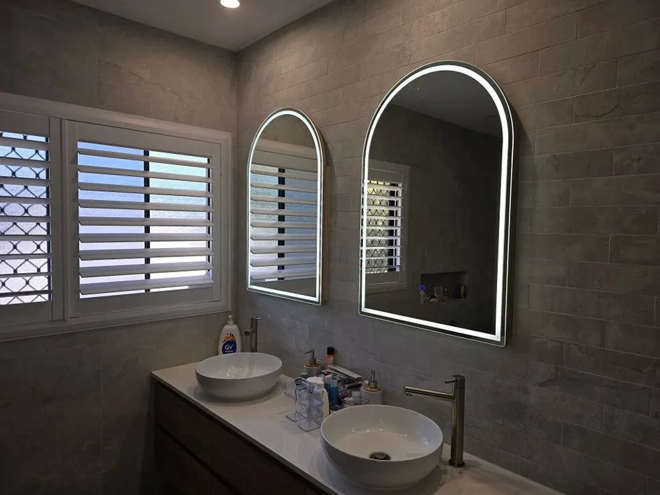 Backlit LED arch mirrors above a modern bathroom vanity